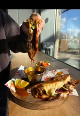 A fast-paced review of a Manchester-based food spot featuring their viral birria ramen, birria tacos, loaded fries, and churros. The video captures the creators' reactions and highlights the food's texture and presentation, specifically focusing on cheese pulls and the dipping experience.