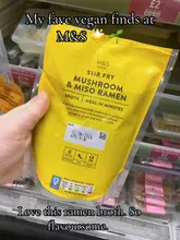 A user-generated photo showcasing a packaged M&S vegan ramen broth product held in front of a supermarket fridge shelf.