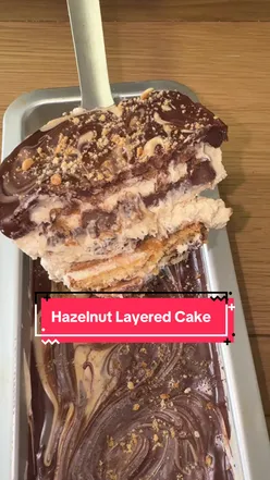 'Indulgent AJ's Hazelnut Layered Cake topped with chocolate drizzle and hazelnuts on a rustic wooden table.'