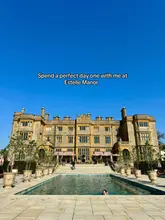 A wide, symmetrical shot of the exterior of Estelle Manor, featuring a large swimming pool in the foreground and the grand stone building in the background under a clear blue sky. The image captures the luxury aesthetic of the venue.