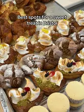 A top-down, close-up shot of a bakery display tray filled with various pastries, including meringue-topped croissants and cookies, used to promote a list of sweet treat spots in Bristol.