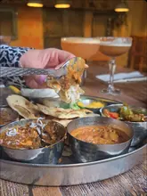 A couple enjoys a variety of Indian dishes and cocktails at Indian Tiffin Room, showcasing a sharing platter and the interactive experience of eating pani puri.