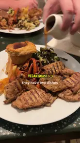 A creator reviews a vegan Sunday roast at a bakery/cafe, highlighting the 'beef' wellington and 'chicken' pieces, along with classic trimmings like Yorkshire puddings and cauliflower cheese. The video includes shots of the food, the venue's interior, and mentions the dog-friendly policy.