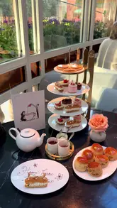 A short, aesthetic montage showcasing an afternoon tea service in a London venue, featuring sandwiches, pastries, scones, and a personalized birthday message on a coffee cup.