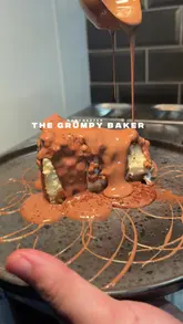 A food review video featuring a creator visiting 'The Grumpy Baker' in Manchester to showcase their range of cheesecakes and desserts, highlighting the indulgent textures and presentation.