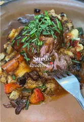 A food review video featuring a visit to Suede in Bradford, showcasing a cocktail, prawn appetizers, sliders, and a lamb shank main course.