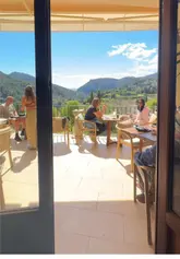 The video is a short, handheld tour of a venue called 'Es Petit,' starting from the entrance, moving through the interior, and ending on a terrace that offers a panoramic view of a valley and town. A person is shown relaxing on the terrace with a drink, highlighting the venue's atmosphere.