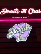 A clean, well-composed photograph of a neon sign for 'Donuts N Chai' mounted on a wooden wall, including the venue's location in Birmingham.
