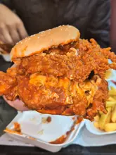 A short, handheld food review video showcasing a double spicy dip chicken burger at 3 in 1 Burger in Birmingham. The video focuses on the size, texture, and sauce of the burger.