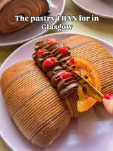 A close-up, high-quality shot of a chocolate and blood orange pastry being sliced with a knife. The image is well-lit, showcasing the texture of the pastry and the glossy finish of the chocolate crémeux, making it highly visually appealing.