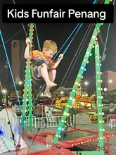 A family travel vlog documenting a visit to a kids' carnival in Batu Ferringhi, Penang. The video features the creator and her son experiencing various rides, including a bungee trampoline, a small roller coaster, and a train ride.