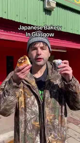 A vlogger visits a Japanese bakery in Glasgow, showcasing the exterior and various baked goods like melon pan, onigiri, and cookies. He provides a taste test of a cinnamon roll and an onigiri, offering his thoughts on the authenticity and taste of the items.