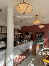 A bright, aesthetically pleasing interior shot of a cafe in Belgravia, London, featuring marble counters, warm lighting, and a stylish, modern design.