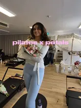 A creator documents their experience at a Pilates event that combines a workout session with a flower arranging workshop, featuring healthy refreshments like chia puddings and wellness shots.