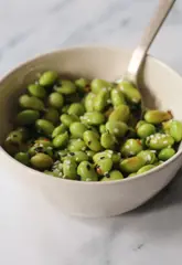 A short, instructional recipe video demonstrating how to prepare edamame beans with soy sauce, sesame oil, and chilli flakes as a high-protein snack.