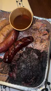 A creator reviews a Texas-style BBQ platter from Texas Taff BBQ, unboxing the meal at home and taste-testing various meats and sides with a friend.