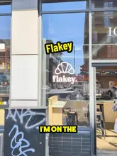 A vlog-style review of Flakey, a cafe located within Ancoats General Store in Manchester, highlighting their £8.50 lunch deal which includes a stuffed croissant and a barista-made drink. The creator samples the beef pastrami croissant and a lavender ube macchiato, providing a positive review of the quality and value.
