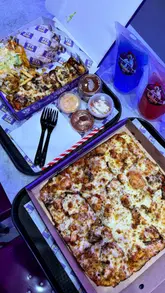 A food review vlog featuring a visit to NYK Fried Chicken in Manchester. The creator walks through the venue, orders a variety of items including a chicken-topped pizza, a burger, loaded fries, and mocktails, and provides a candid review and rating of the food.