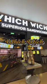 Two creators visit a Which Wich sandwich shop in Cardiff, demonstrating the ordering process using kiosks and paper bags, and reviewing their chosen sandwiches, sides, and drinks.
