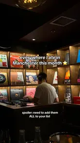 A moody, atmospheric shot of a DJ at a mixing desk in a bar with a wall of vinyl records, used as a cover image for a listicle about Manchester dining spots.