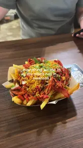 A food review video featuring a visit to Albert Hall in Swansea, where the creator samples loaded fries, a pork gyros, a smash burger, and a chicken burger, providing brief commentary on each.