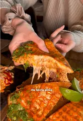 A creator visits Taco House in Hackney, London, to review their viral birria pizza. The video features a variety of shots including close-ups of the food, the venue's interior, and the canal-side outdoor seating area. The creator provides a voiceover review while sampling the food, including loaded fries, honey barbecue wings, and a smash burger.