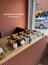 A clear, well-lit photograph of a bakery display case filled with various pastries, including kouign amann, cardamom buns, and almond croissants. The image is taken from a slightly elevated angle, showcasing the selection available to customers.