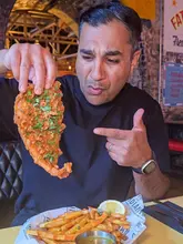 A creator reviews the Indian Fish and Chips at the Indian Brewery in Birmingham. The video features close-up shots of the food, including the dipping of the fish into a curry sauce, and highlights the venue's own brewed beers and casual atmosphere.