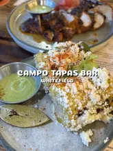 A short, music-led montage showcasing a new Latin American menu at Campo Tapas Bar in Manchester. The video features close-up shots of various dishes including lamb barbacoa tacos, marinated grilled chicken, roasted seabass, and charred corn, alongside cocktails.