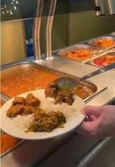 A first-person POV video showcasing a visit to an all-you-can-eat Indian buffet restaurant. The creator walks along the buffet line, plating up a variety of dishes including curries, starters, and desserts, while providing a voiceover commentary on the food selection.