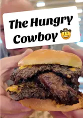 The creator visits 'The Hungry Cowboy' at Tiger Yard, providing a review of their BBQ-style street food. The video features close-ups of smash burgers, loaded fries, nachos, and mac and cheese, while explaining the venue's QR code ordering system and highlighting the casual, social atmosphere.