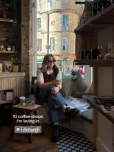 A cozy, aesthetic shot of a person sitting in a window seat at an Edinburgh coffee shop, holding a green drink. The image captures a relaxed, solo-visit vibe typical of coffee shop content.