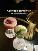 A high-quality, moody shot of two cocktails on a table, illuminated by a stylish gold lamp, promoting a bar located in the National Portrait Gallery.