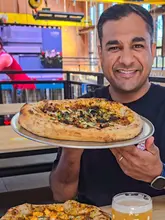 A creator reviews Indian-inspired pizzas at The Indian Brewery Taproom, highlighting the unique fusion flavours like butter paneer and butter chicken, while also showcasing the venue's amenities including pool tables, dart boards, and live sports screens.