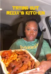 A creator reviews a takeaway meal from Reeka's Kitchen while sitting in her car, discussing the quality of the wings, mac and cheese, plantain, and jollof rice.