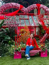 A creator poses in front of a vibrant floral display at the Chelsea Flower Show, with text overlay indicating the content is a guide to the event.