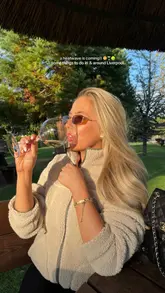 A high-quality, lifestyle-focused shot featuring a woman enjoying a glass of white wine in an outdoor garden setting, likely at a pub or bar in Liverpool. The image uses warm, golden hour lighting to create an aspirational and inviting atmosphere, effectively promoting summer socialising.