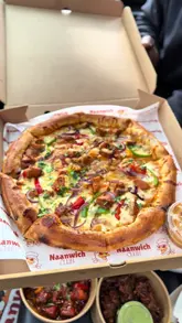 A food review vlog where the creator visits Naanwich Club, a takeaway spot in a car park, and samples several items including a butter chicken naan wrap, butter chicken pizza, onion bhajis, and chicken pieces.