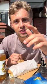 A creator reviews sandwiches from CJ's Sandwich Shop in Whalley, showcasing a bacon and sausage butty and a salmon baton while sitting outside the venue.