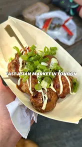 A short, energetic vlog showcasing a visit to an East Asian market at the Urban Garden Fair in Canary Wharf. The video highlights various food stalls, including takoyaki, katsu curry, and dumplings, while capturing the sunny, riverside atmosphere and the presence of market stalls and pets.