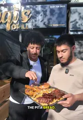 Two creators review a large food platter at Taqi's Grill in Birmingham, showcasing the peri-peri chicken, doner, smash burger, rice, and fries, while highlighting the venue's atmosphere.