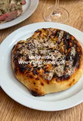 A concise and visually appealing review of a Manchester wine bar, highlighting the interior, wine selection, and several small plates including flatbread, roast lamb, pork chop, and dessert.