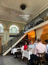A high-quality, atmospheric shot of a dining table at Session Arts Club in London, capturing the elegant, rustic interior design and the social dining experience.