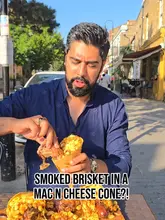 A creator reviews the 'Cone Carnage' at The Axe & Ember Smokehouse, featuring smoked brisket, back ribs, and sausage served in a mac and cheese-filled cone.