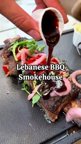 A review of a Lebanese-inspired BBQ smokehouse in Brixton, featuring a variety of grilled meats including lamb chops, lamb shank, whole chicken, and beef ribs, alongside a falafel platter. The video highlights the smoky flavors and tender textures of the food.