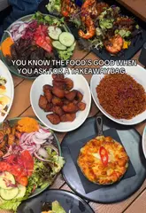 A short, energetic video featuring a group of friends enjoying a spread of Afro-Caribbean food, specifically highlighting Suya and other sides, ending with them getting a takeaway bag.