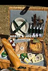 A couple enjoys a picnic in a park using a takeaway picnic basket service provided by The Horse & Jockey in Chorlton. The video showcases the various items included in the basket, such as artisan baguettes, local cheeses, pickles, and desserts, while demonstrating the convenience of the provided crockery and cutlery.
