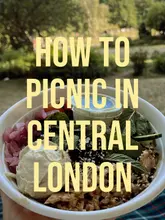 A vibrant, healthy salad bowl from Urban Greens, presented as a picnic option in Central London. The image features a fresh, colourful bowl held in a hand against a blurred park background, highlighting the ingredients like hummus, chicken, and fresh herbs.