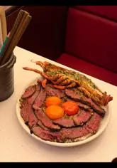 A creator reviews a limited-edition Surf and Turf rice bowl at a restaurant, featuring 40-day aged beef and a lobster tail. The video includes close-up shots of the food preparation and the creator's reaction.