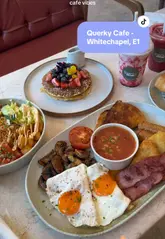A short, aesthetic montage showcasing a variety of breakfast and brunch dishes at Querky Cafe in Whitechapel, London. The video features close-ups of an English breakfast, a halloumi bowl, a salmon and cream cheese bagel, pancakes, and smoothies, interspersed with brief shots of the cafe interior.